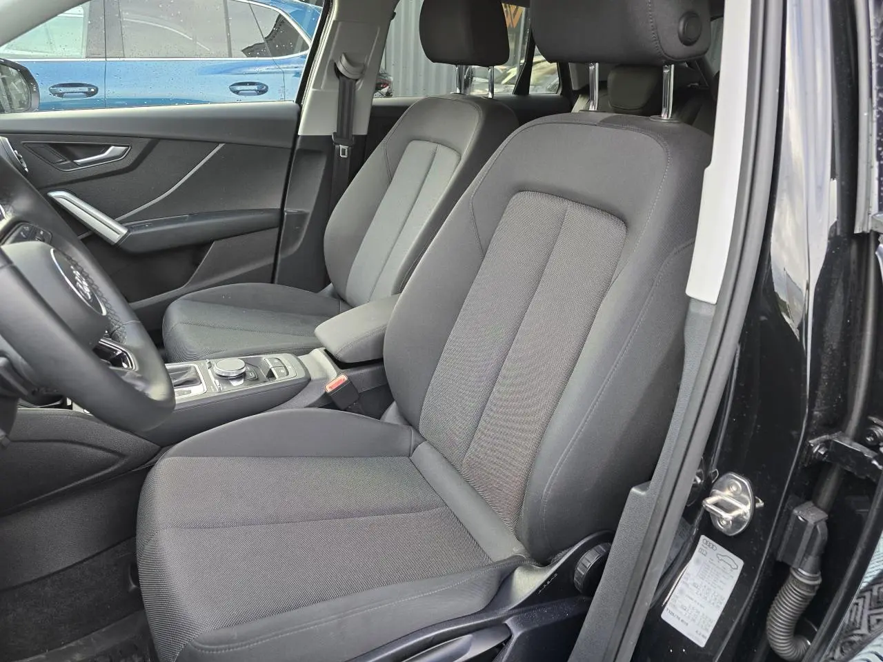 Vue intérieure côté conducteur de l'Audi Q2 35 TFSI 2023 noir mythic, sièges tissu gris et console centrale visible.