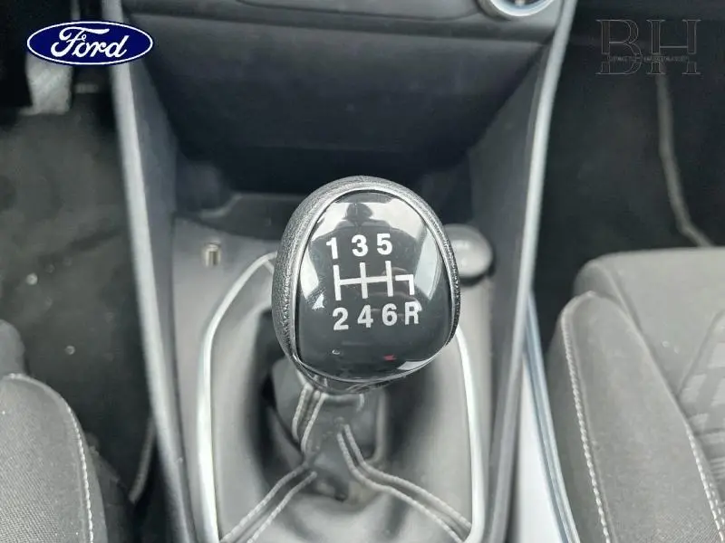 Gros plan sur le levier de vitesses manuel noir de la Ford Fiesta Titanium Business blanche, entouré de sièges tissu noir.