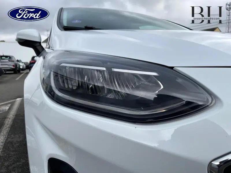 Gros plan sur le phare avant droit d'une Ford Fiesta blanc glacier 2022, soulignant son design moderne et précis.
