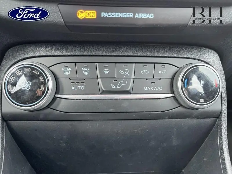 Vue rapprochée de la console centrale de la Ford Fiesta blanche, montrant les commandes de climatisation automatique et l'indicateur airbag passager.