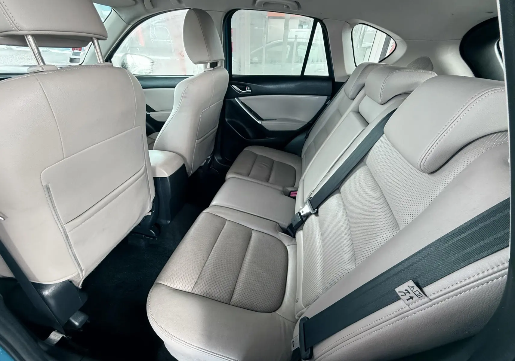 Vue intérieure arrière montrant les sièges en cuir beige du Mazda CX-5 bleu, avec ceintures de sécurité visibles.
