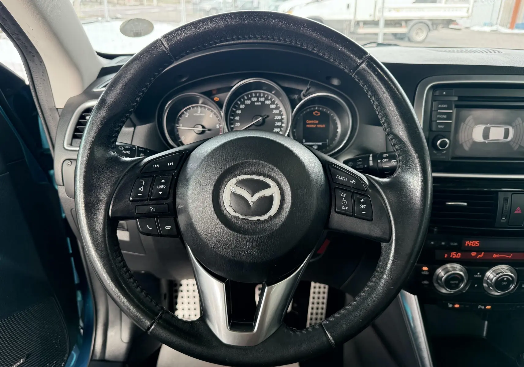 Vue intérieure centrée sur le volant en cuir noir du Mazda CX-5 bleu 2013 avec tableau de bord et écran multimédia visible.