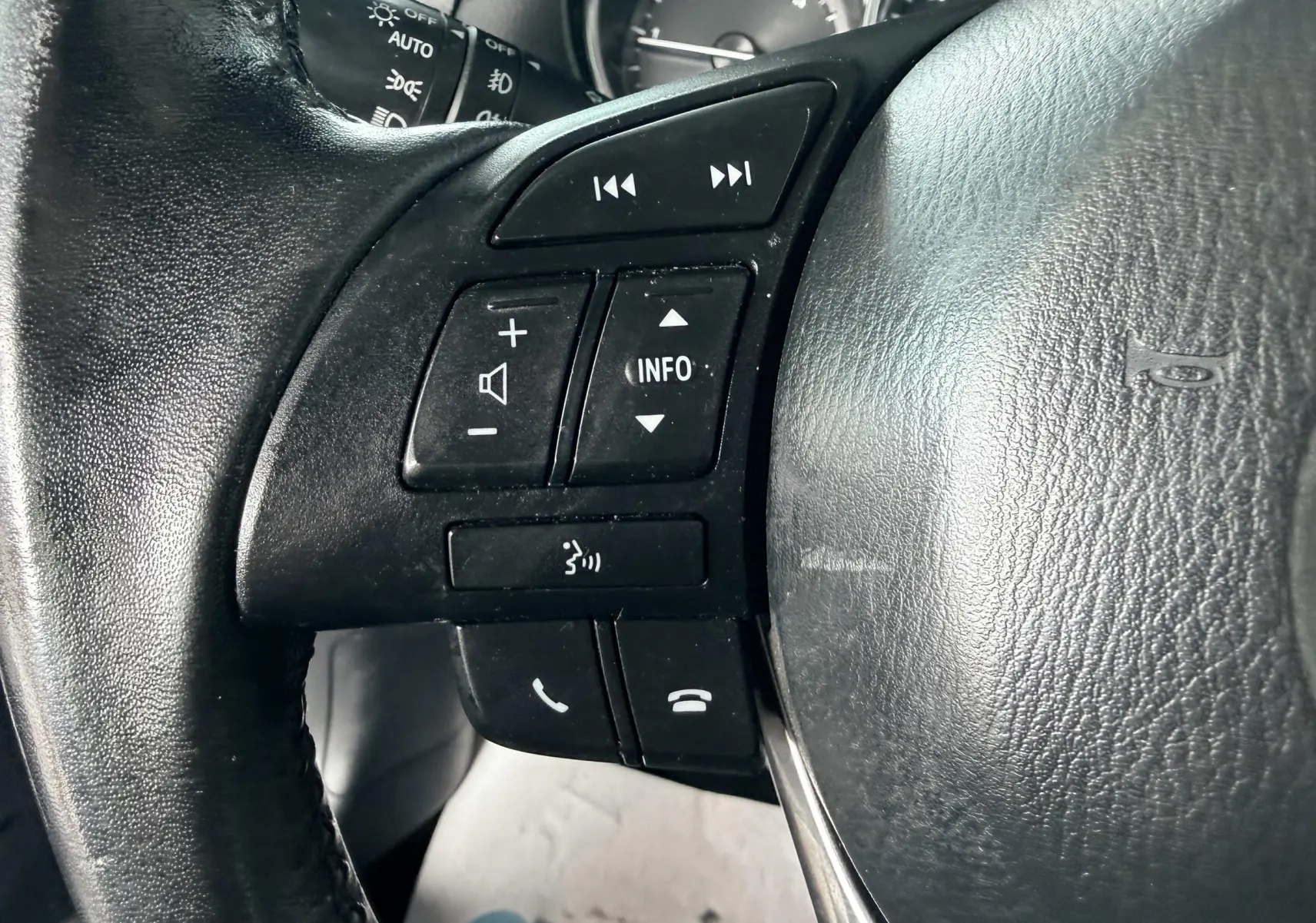 Gros plan sur les commandes du volant noir du Mazda CX-5 2013, avec boutons audio et téléphone intégrés.