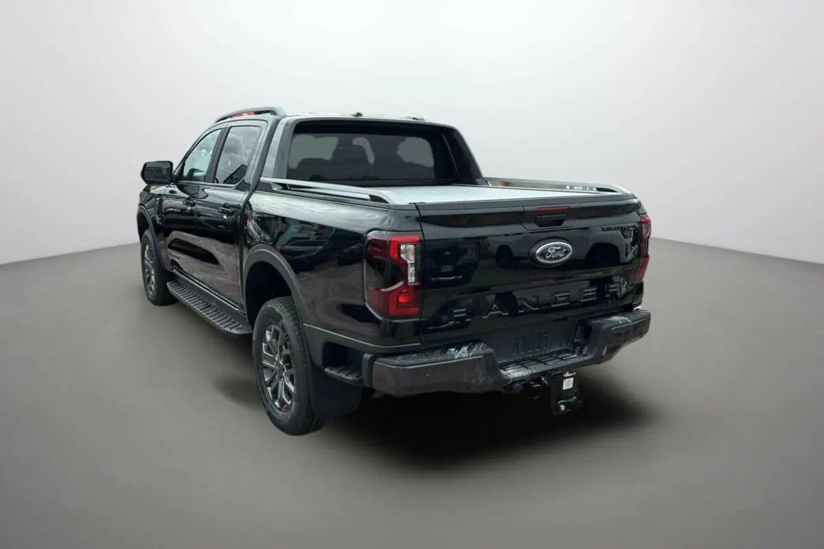 Ford Ranger 2025 noir agate vu 3/4 arrière droit avec attelage et barres de toit visibles.