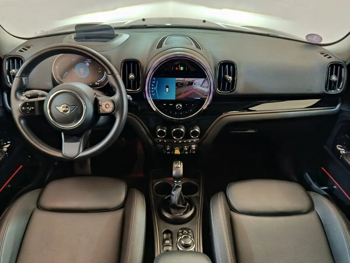 Vue intérieure frontale du tableau de bord noir du MINI Countryman Cooper SE avec écran tactile circulaire et volant cuir.