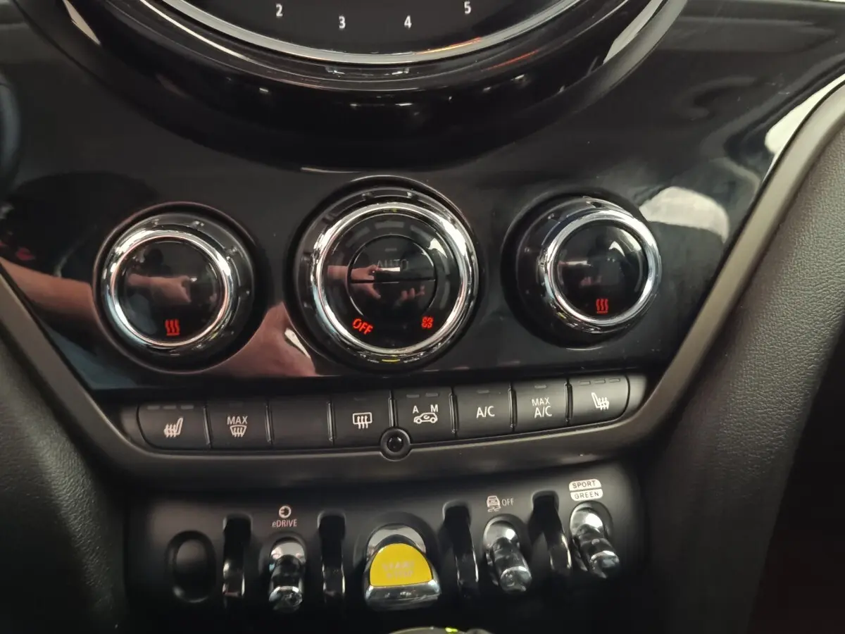 Gros plan sur la console centrale noire du MINI Countryman 2023 avec commandes climatisation et bouton start/stop jaune.