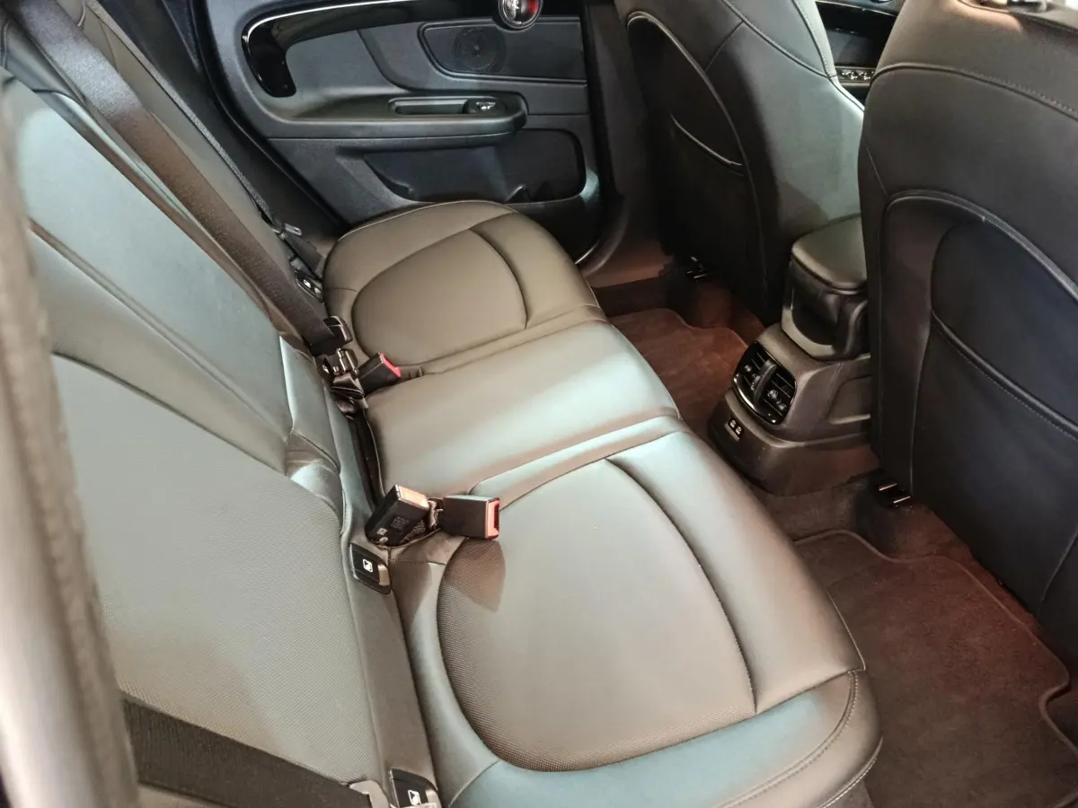 Vue intérieure arrière côté gauche du MINI Countryman Cooper SE Essential 2023, sièges cuir noirs et console centrale avec aérateurs.