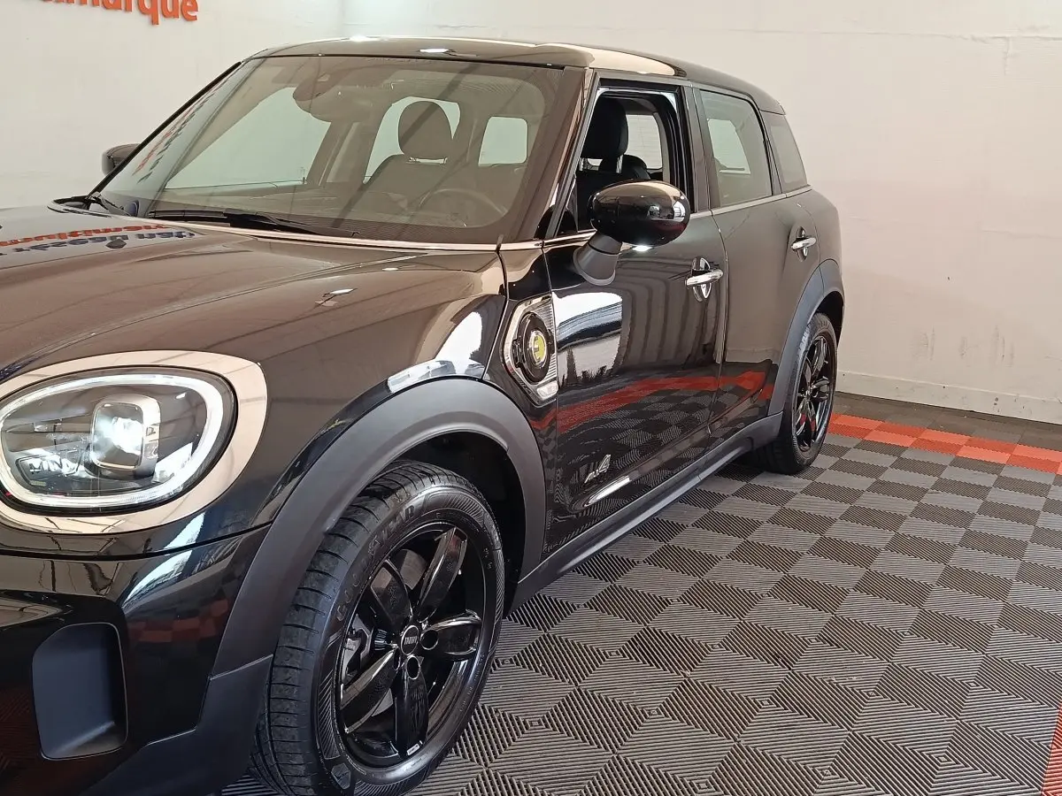 Vue 3/4 avant droit d'une MINI Countryman Cooper SE noire avec jantes noires et logo électrique sur l'aile.