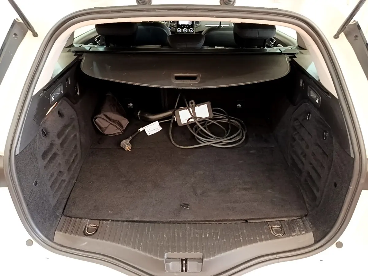Coffre ouvert d’une Renault Mégane Business E-Tech hybride blanche, avec câble de recharge visible et cache-bagages déployé.