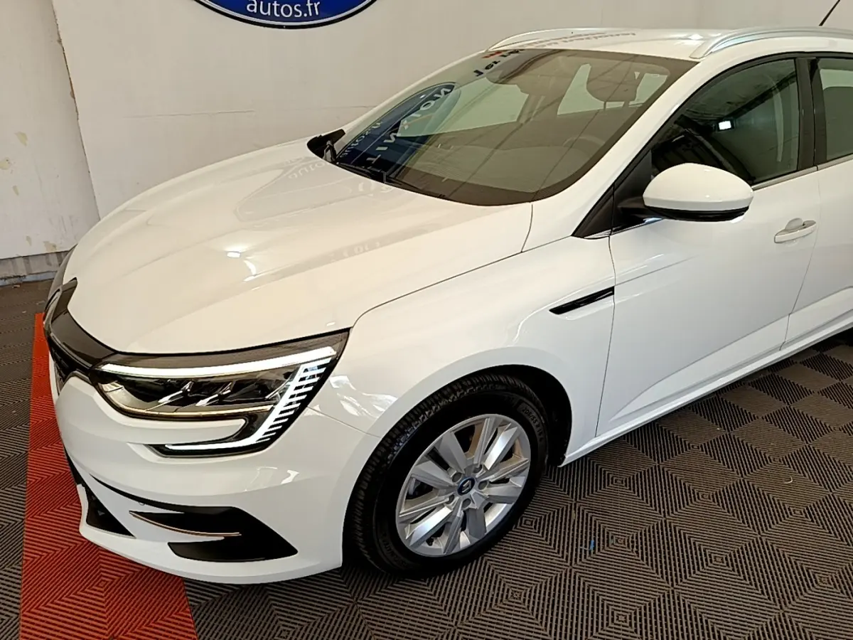 Vue 3/4 avant droite d'une Renault Mégane Business E-Tech hybride rechargeable blanche avec feux LED distinctifs et jantes alliage.
