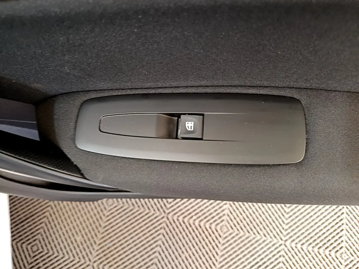 Gros plan sur le bouton de commande de la vitre électrique côté conducteur dans une Renault Mégane blanche hybride rechargeable.