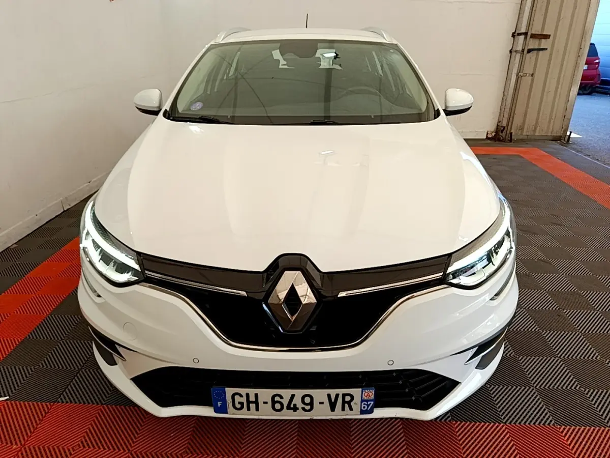 Vue avant d'une Renault Mégane Business E-Tech hybride rechargeable blanche avec phares LED allumés dans un garage.