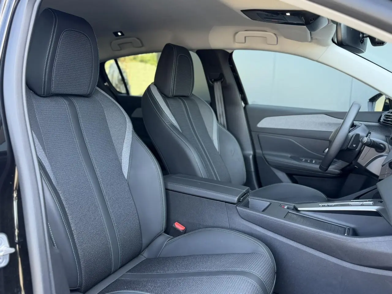 Vue intérieure côté gauche des sièges avant en sellerie tri matières TEP/tissu gris et noir de la Peugeot 308 Hybrid 2025.