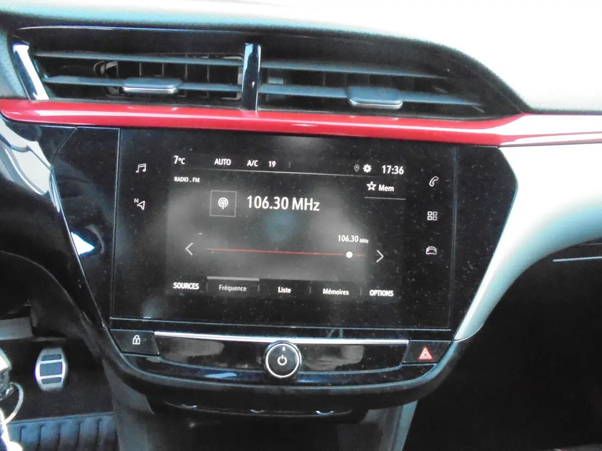 Tableau de bord de l’Opel Corsa gris quartz, avec écran tactile radio affichant 106.30 MHz et bandeau rouge décoratif.