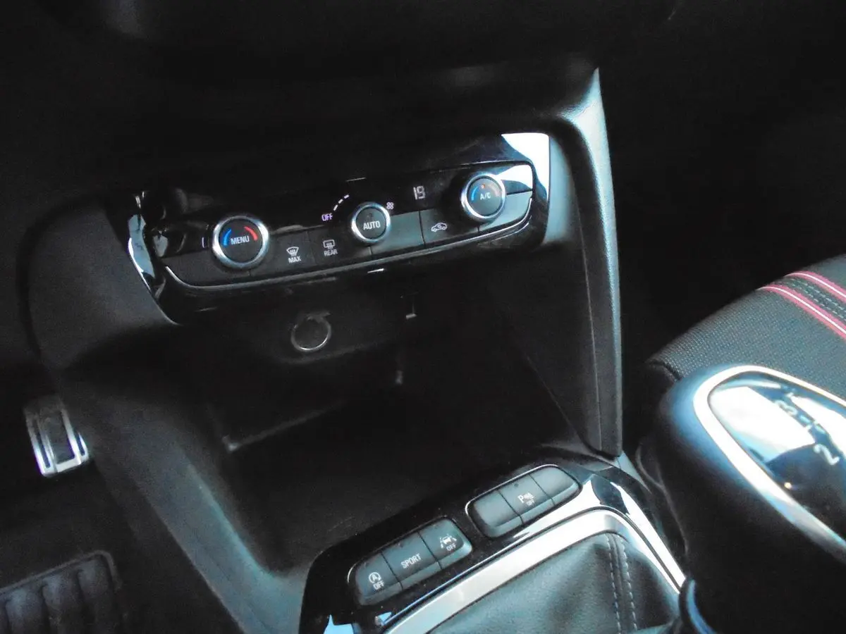 Gros plan sur la console centrale et commandes climatisation d'une Opel Corsa gris quartz, intérieur noir avec surpiqûres rouges.