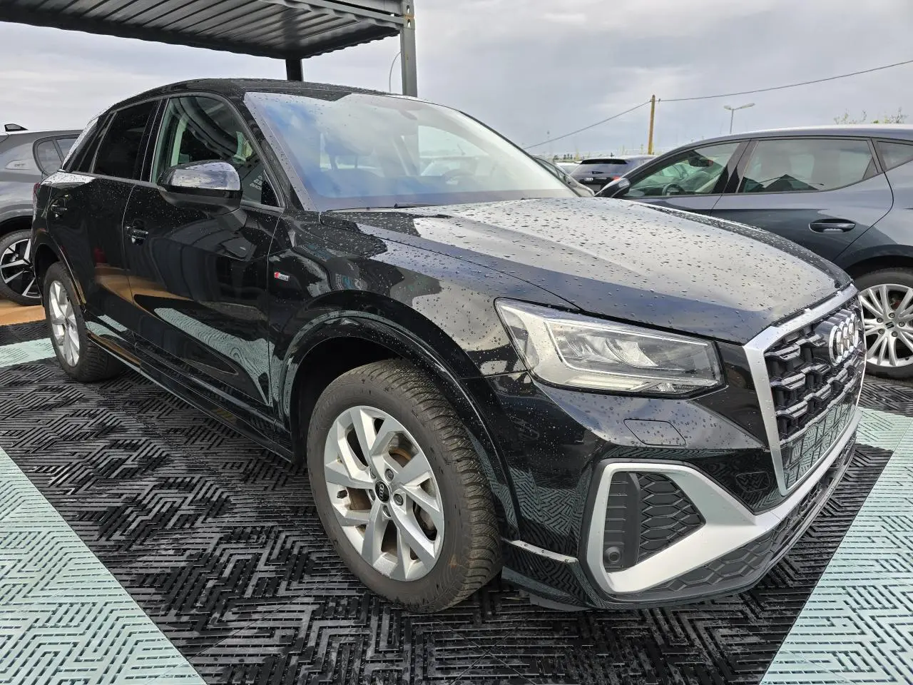 Audi Q2 noir mythic vue 3/4 avant droit sous pluie avec jantes aluminium et calandre S-Line sportive
