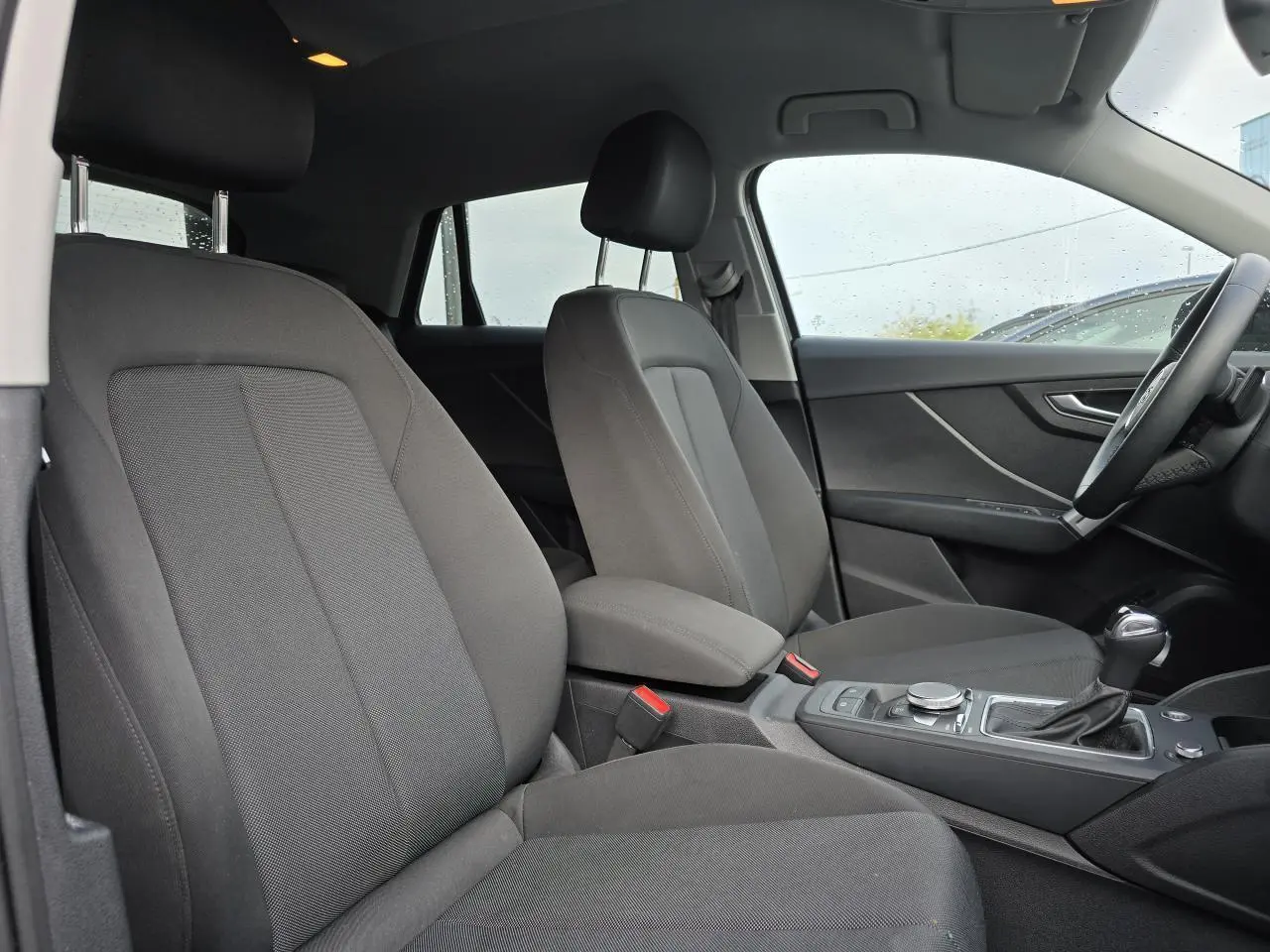 Vue intérieure côté conducteur de l'Audi Q2 2023 avec sièges tissu gris et console centrale équipée d'une boîte automatique.
