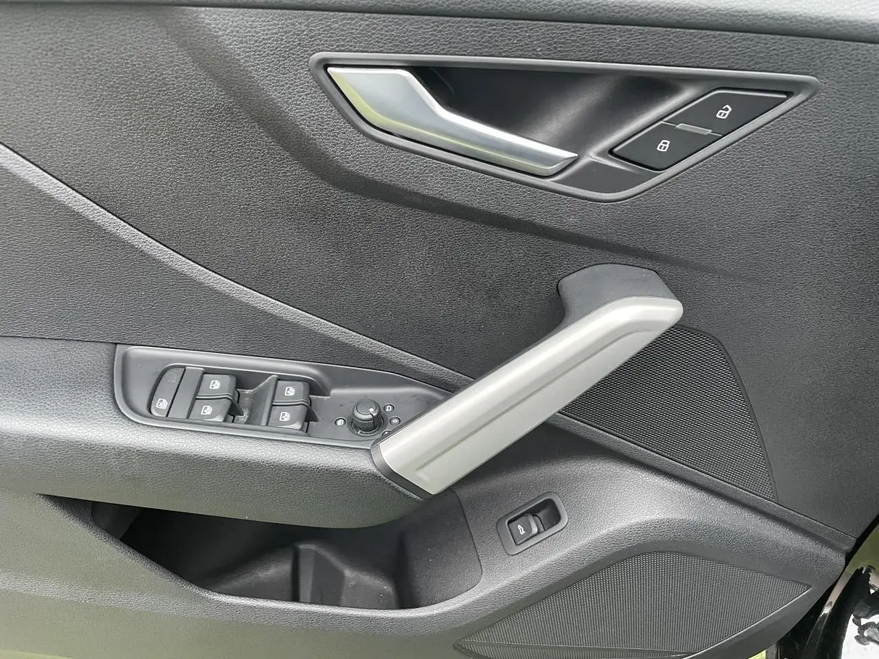 Détail de la porte avant gauche de l'Audi Q2 noir mythic, avec commandes de vitres et poignée argentée.