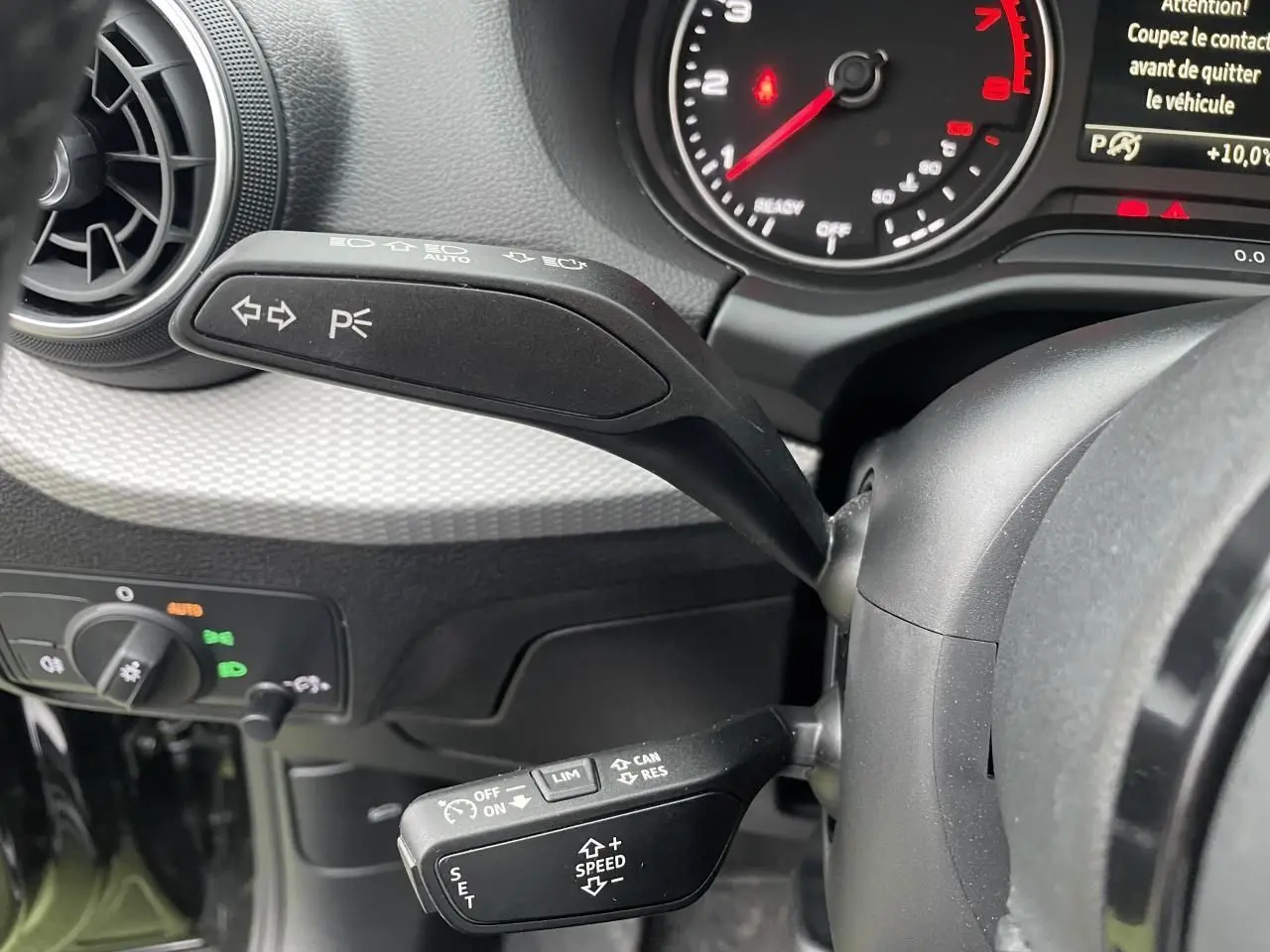Gros plan sur les commandes au volant d’un Audi Q2 2023 noir mythic, avec levier clignotant et régulateur de vitesse.