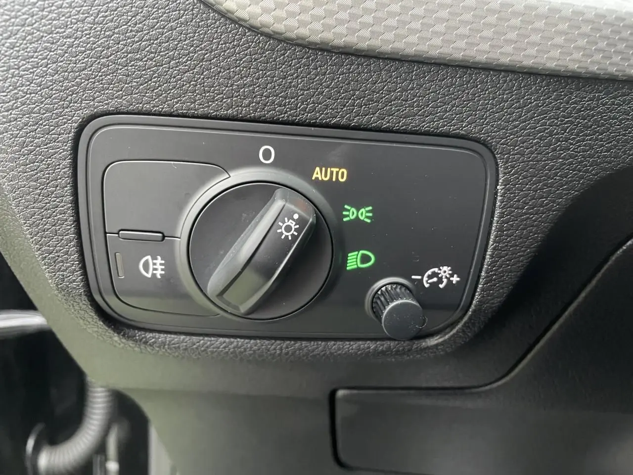Gros plan sur le bouton de commande des phares avec réglage automatique dans l'Audi Q2 noir Mythic 2023.