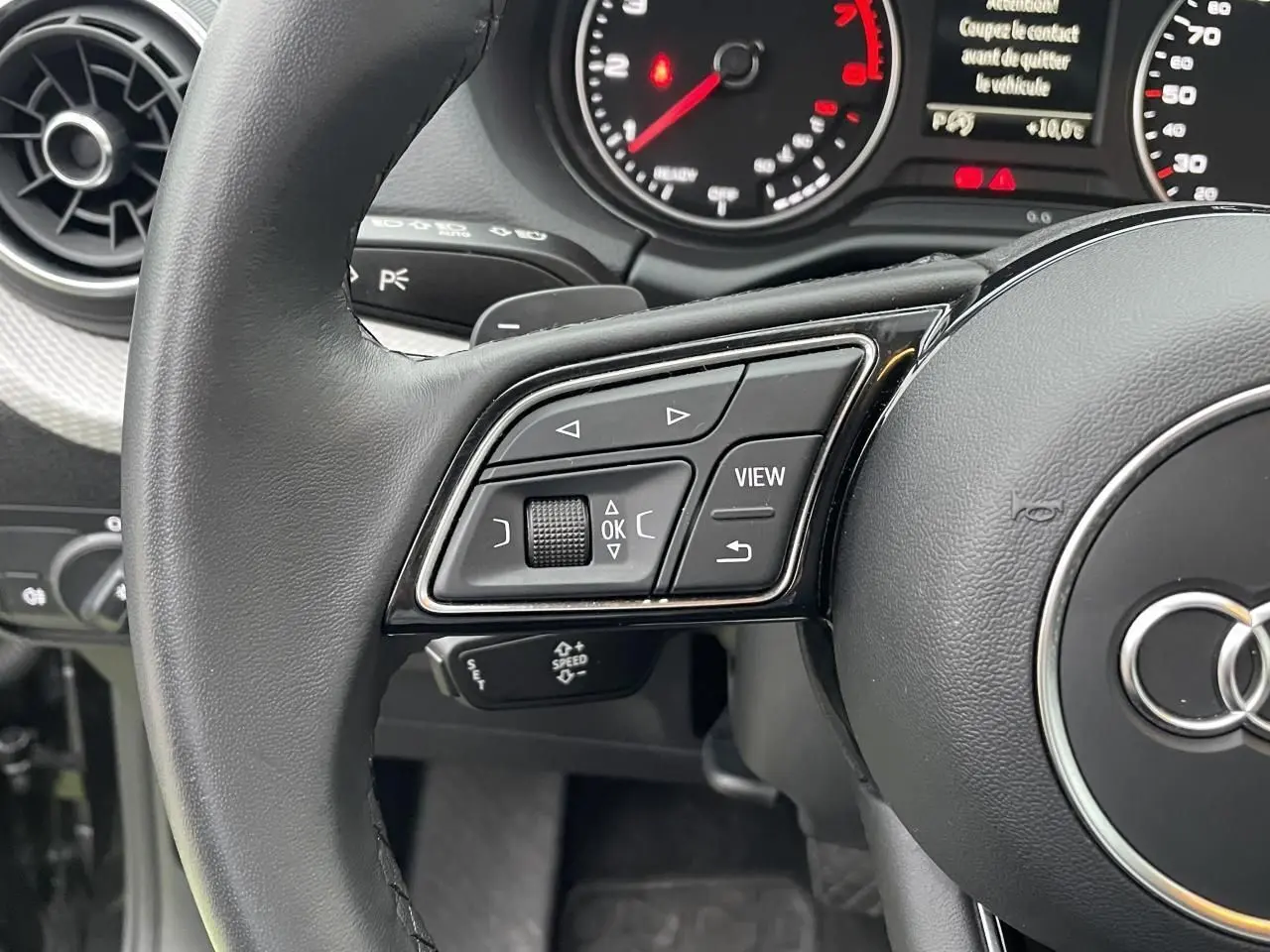 Gros plan sur le volant multifonction noir de l'Audi Q2 35 TFSI 2023 avec commandes intégrées et tableau de bord partiel.