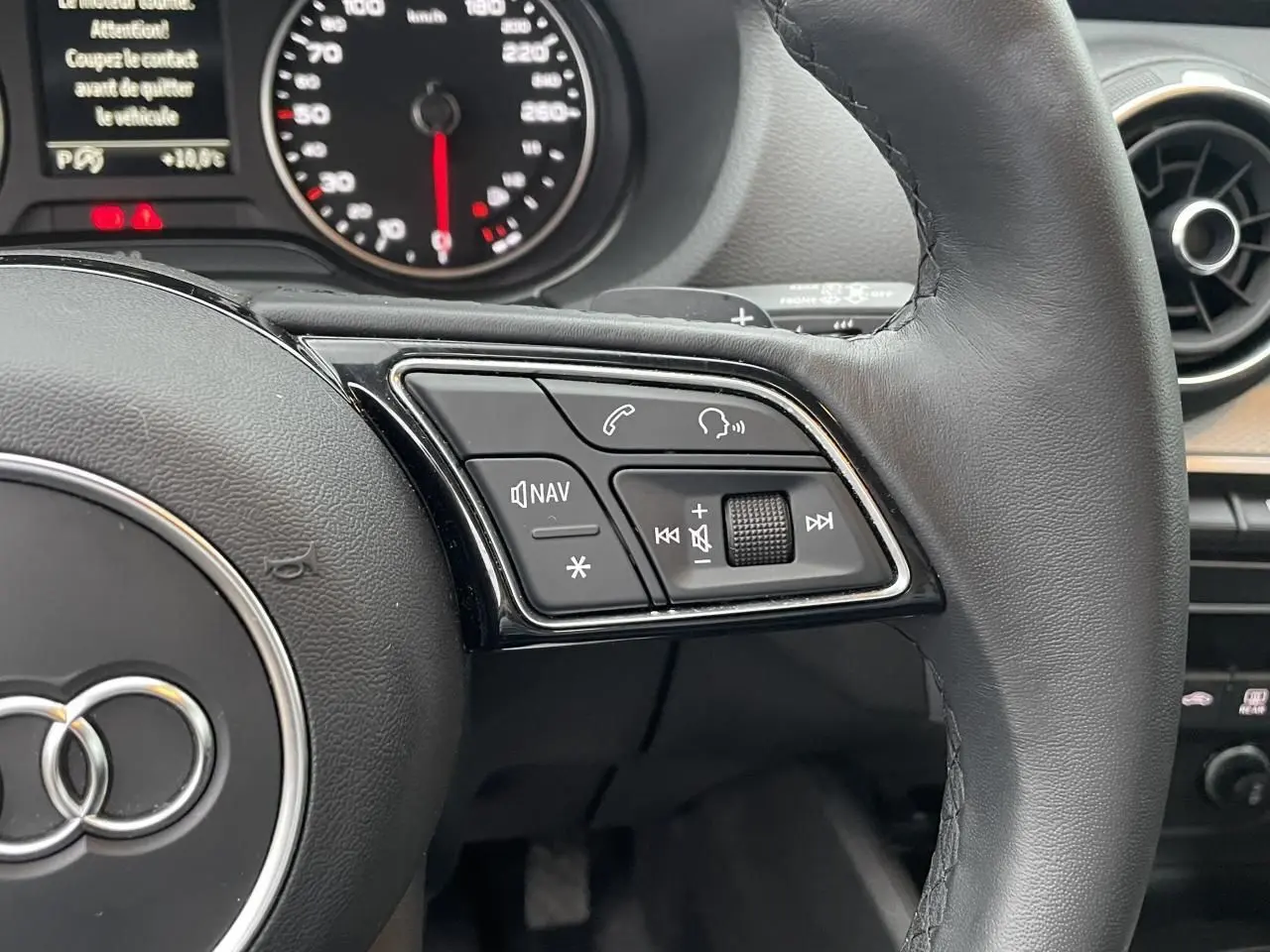 Gros plan sur le volant cuir noir de l'Audi Q2 2023, avec commandes multifonctions et tableau de bord partiel visible.