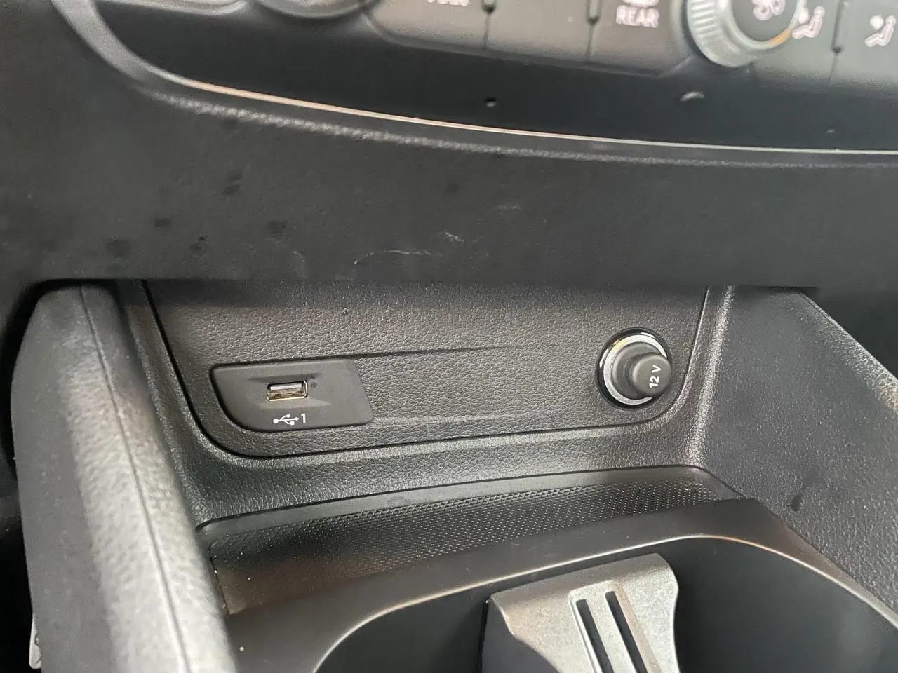 Gros plan sur la console centrale noire de l'Audi Q2 2023, avec prise USB et allume-cigare 12V visibles.