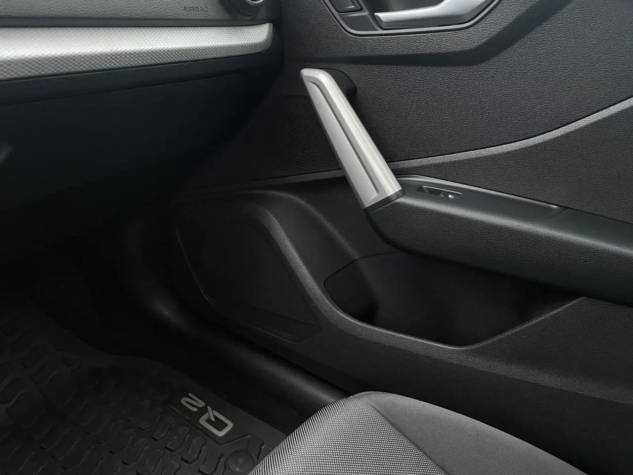 Détail intérieur côté passager de l'Audi Q2 2023, montrant la porte avec poignée argentée et tapis de sol marqué Q2.