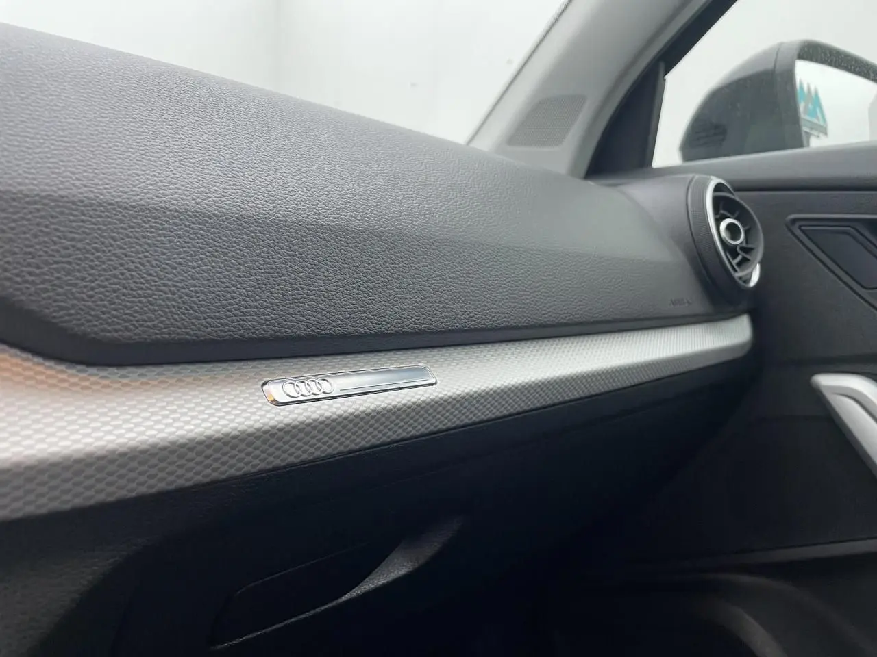 Détail de la planche de bord côté passager de l'Audi Q2 35 TFSI 2023 avec insert décoratif argent et sortie d'air ronde.