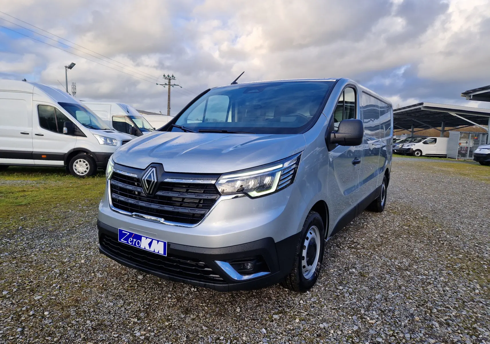 Renault Trafic Fourgon gris Highland en 3/4 avant droit, avec calandre noire et phares LED allumés.