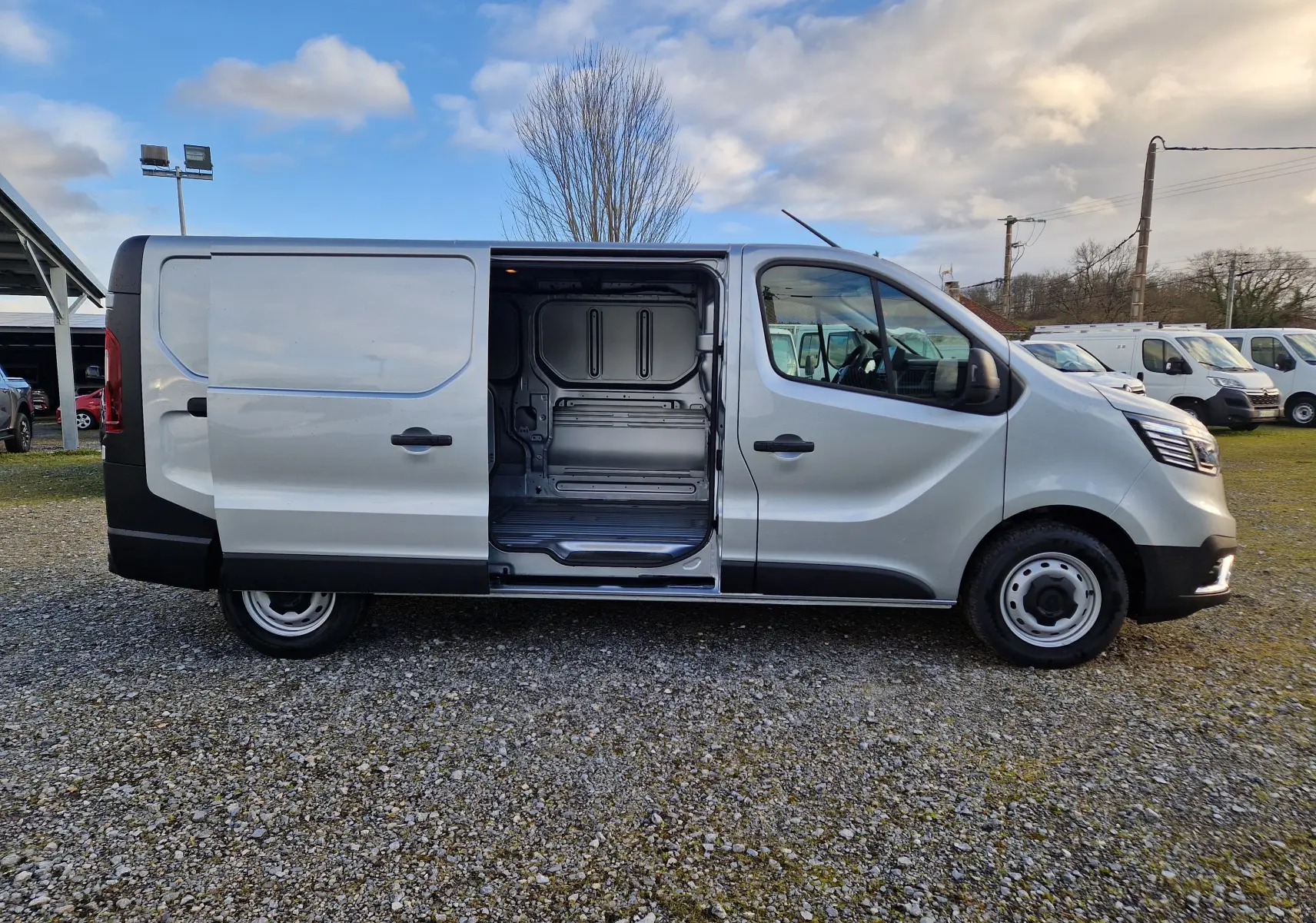 Vue latérale droite d'un Renault Trafic Fourgon gris Highland avec porte coulissante ouverte montrant l'espace de chargement vide.