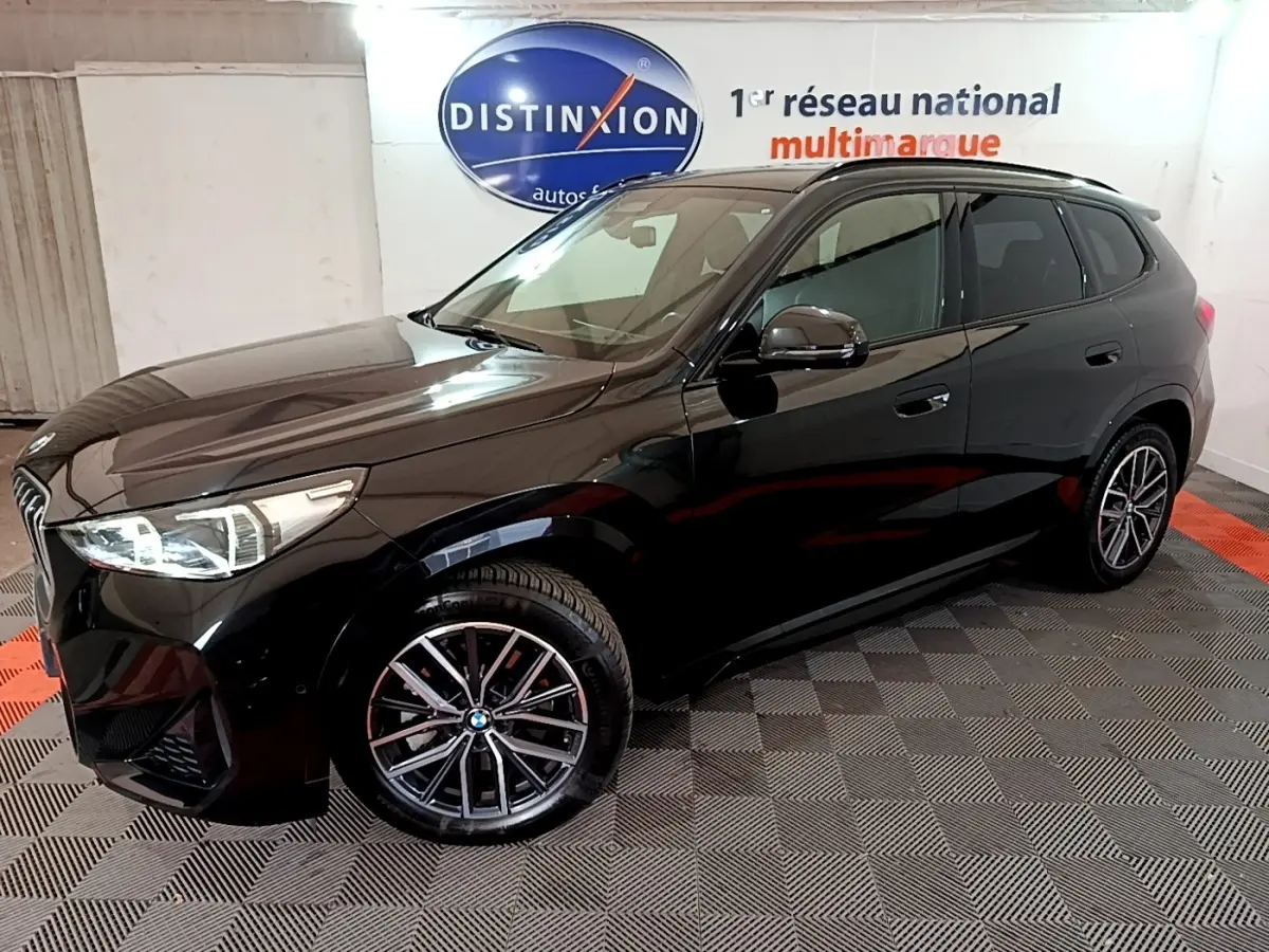 BMW X1 xDrive23i M Sport noir en 3/4 avant droit, avec jantes alliage et phares LED visibles en intérieur showroom