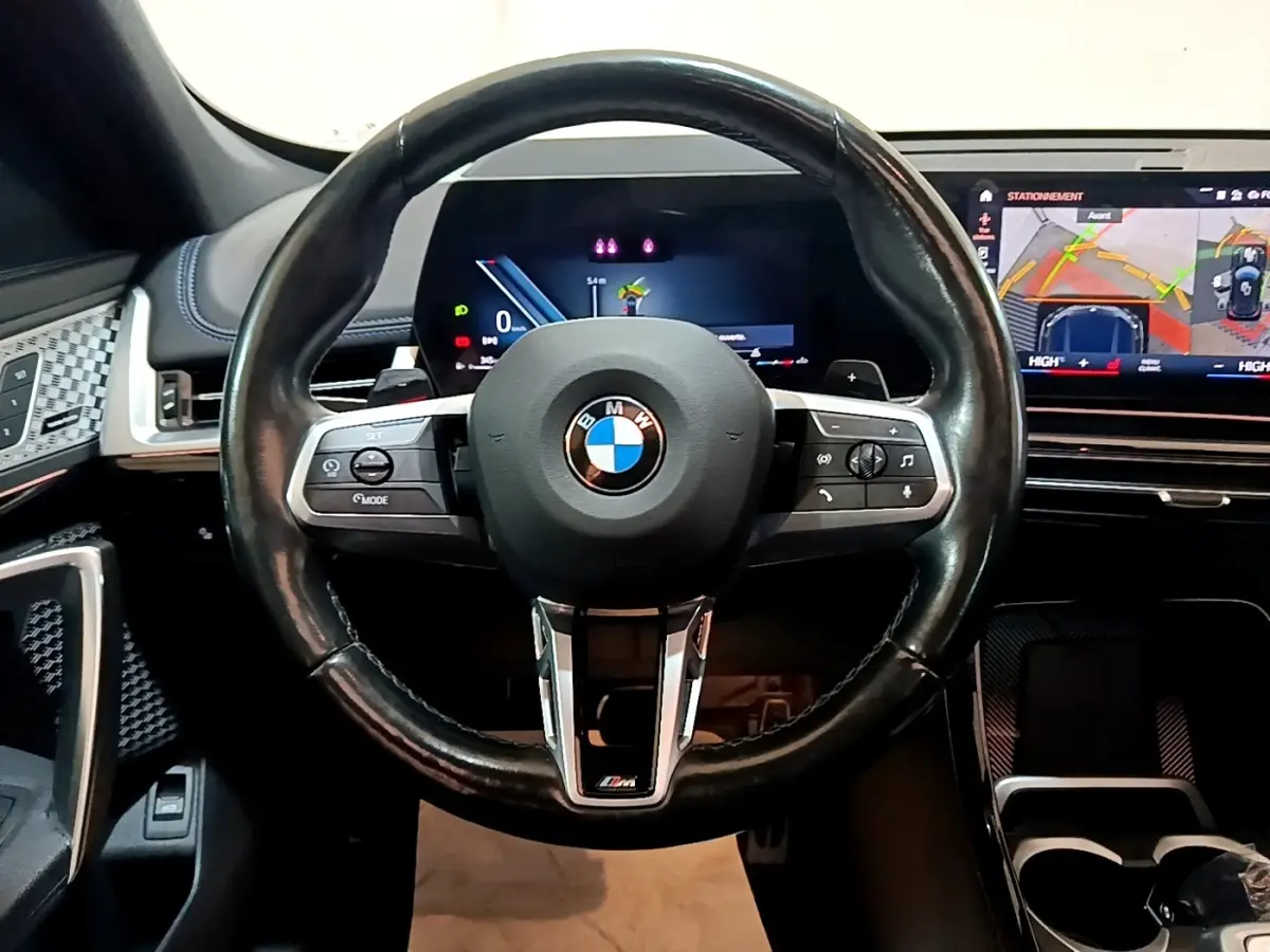 Volant cuir noir BMW X1 xDrive23i M Sport 2023 vu de face avec tableau de bord digital et écran tactile de navigation.
