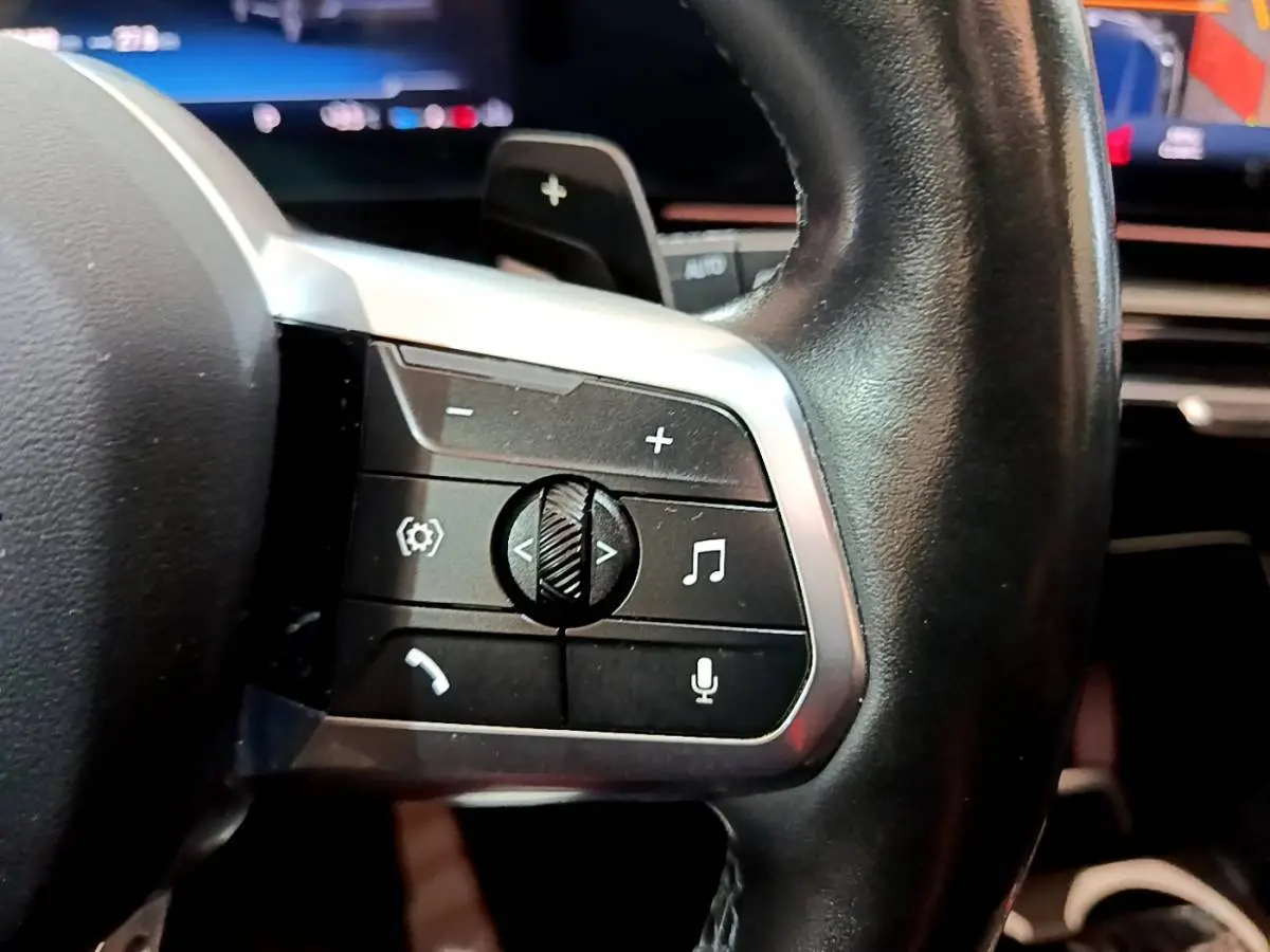 Gros plan sur la partie gauche du volant cuir noir du BMW X1 xDrive23i M Sport 2023 avec commandes audio et vocales.