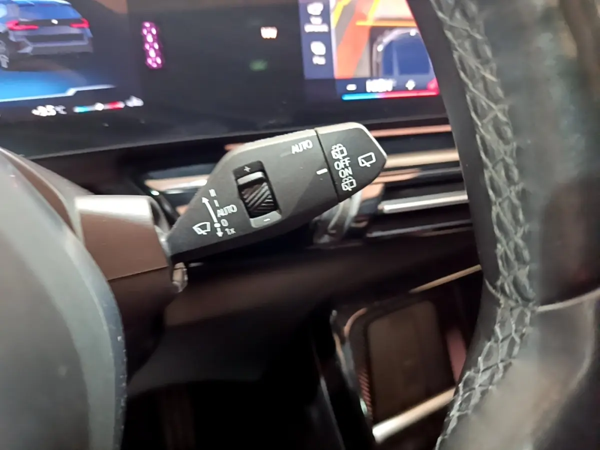 Gros plan sur la commande d’essuie-glace à gauche du volant cuir d’une BMW X1 noire, avec tableau de bord numérique en arrière-plan.