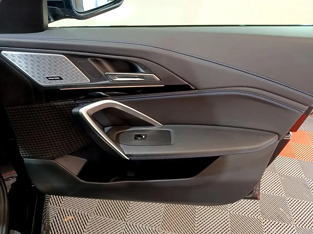 Détail de la porte côté gauche noire du BMW X1 2023 avec surpiqûres bleues et haut-parleur Harman Kardon intégré.