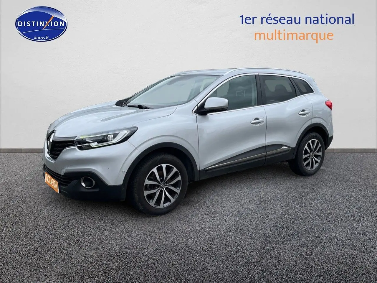 Renault Kadjar gris platine en 3/4 avant droit, avec jantes alliage et barres de toit visibles.