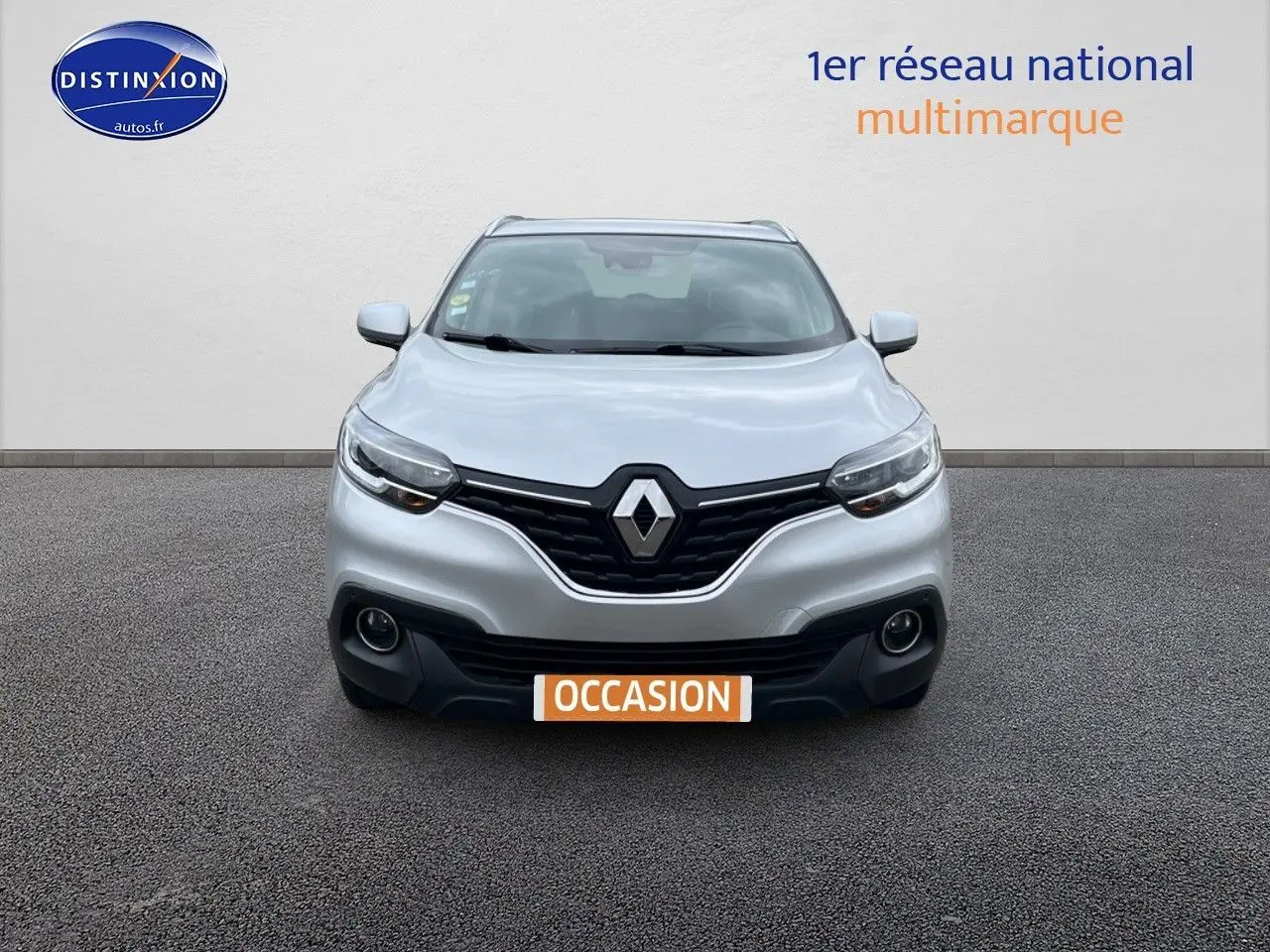 Vue frontale d'un Renault Kadjar gris platine avec calandre noire et phares allumés sur fond neutre.