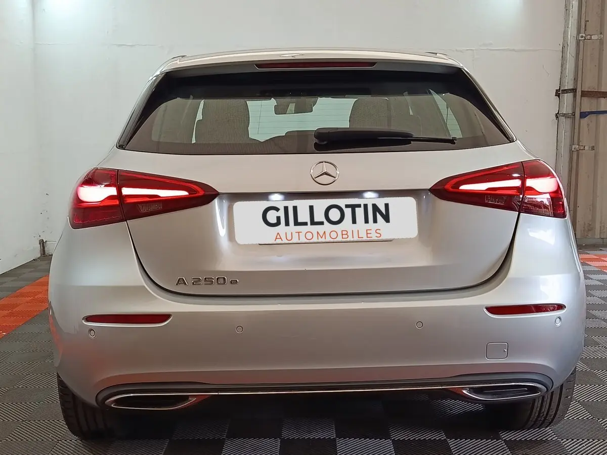 Vue arrière d'une Mercedes Classe A 250 e hybride rechargeable gris clair avec feux LED allumés en intérieur.