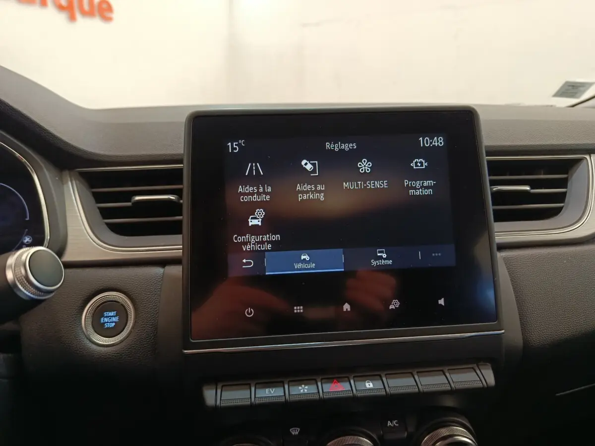 Vue rapprochée de l’écran tactile central et du bouton démarrage du tableau de bord du Renault Captur Intens E-TECH gris clair.