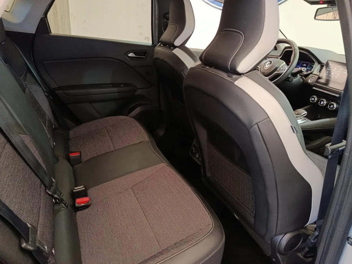 Vue intérieure côté arrière droit du Renault Captur Intens E-TECH 2021, sièges tissu gris et noir avec tableau de bord visible.