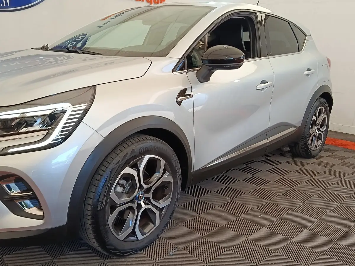 Vue 3/4 avant droit d'un Renault Captur Intens E-TECH gris clair avec jantes alliage et feux LED allumés.