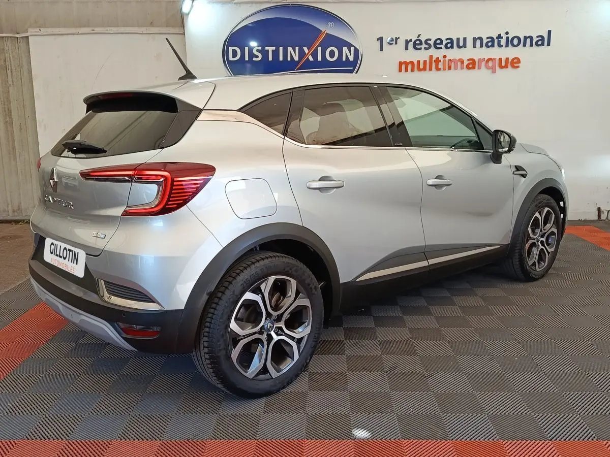 Vue 3/4 arrière droite d’un Renault Captur Intens E-TECH gris clair avec jantes alliage et vitres teintées.