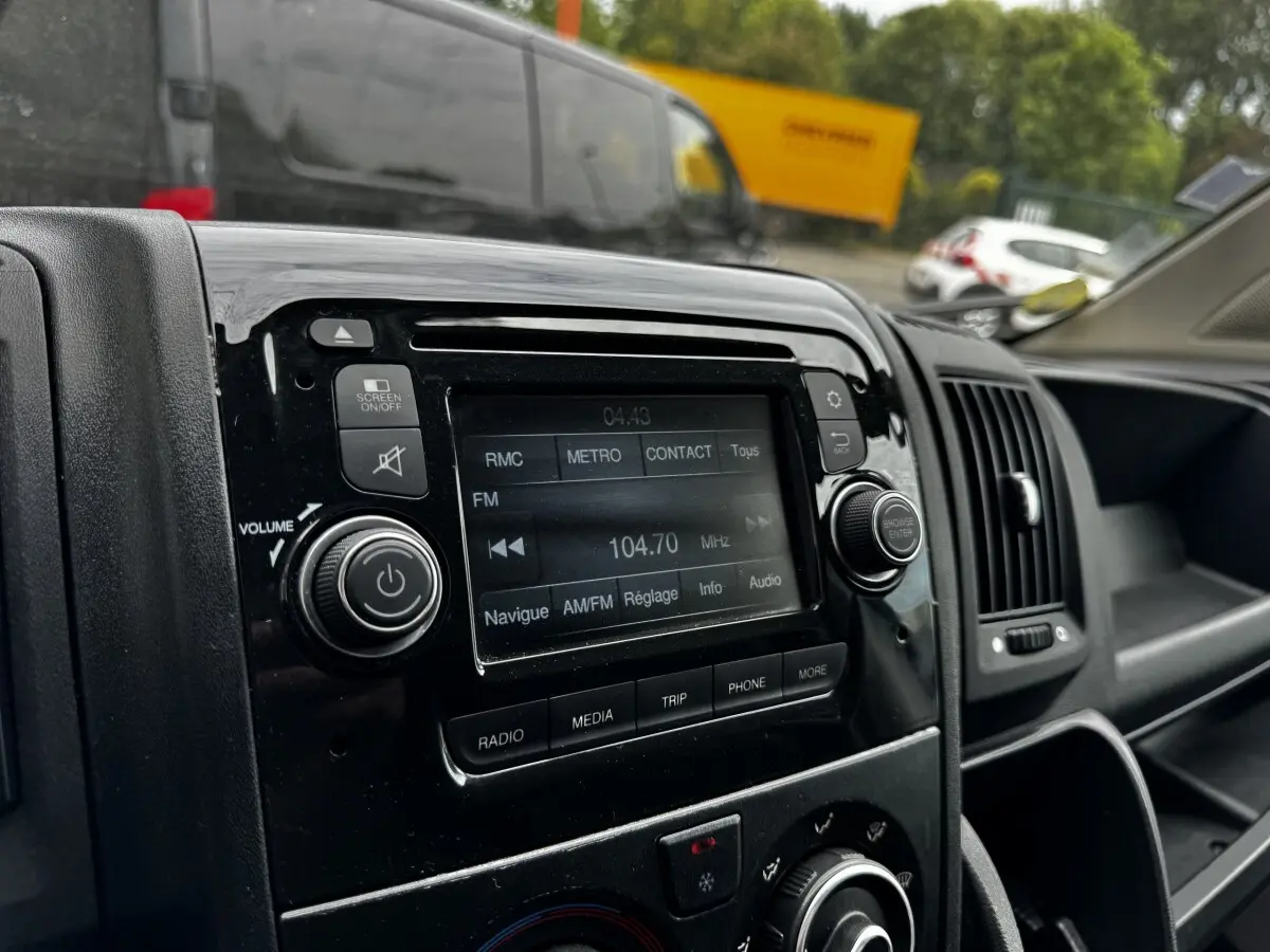 Gros plan sur la console centrale noire du Citroën Jumper blanc, affichant l’écran tactile radio FM à 104,7 MHz.
