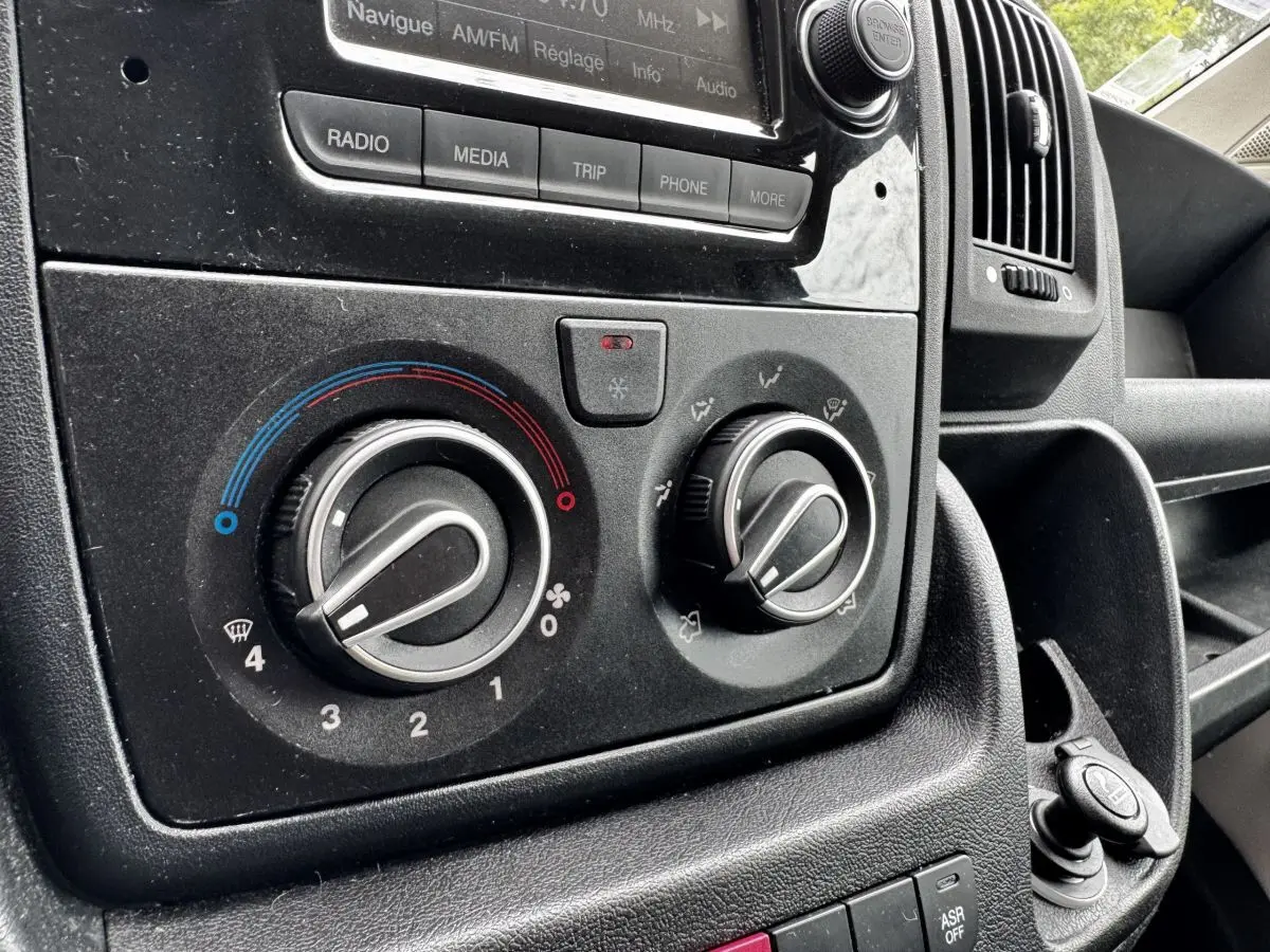 Gros plan sur les commandes de climatisation et radio du tableau de bord noir du Citroën Jumper blanc de 2019.
