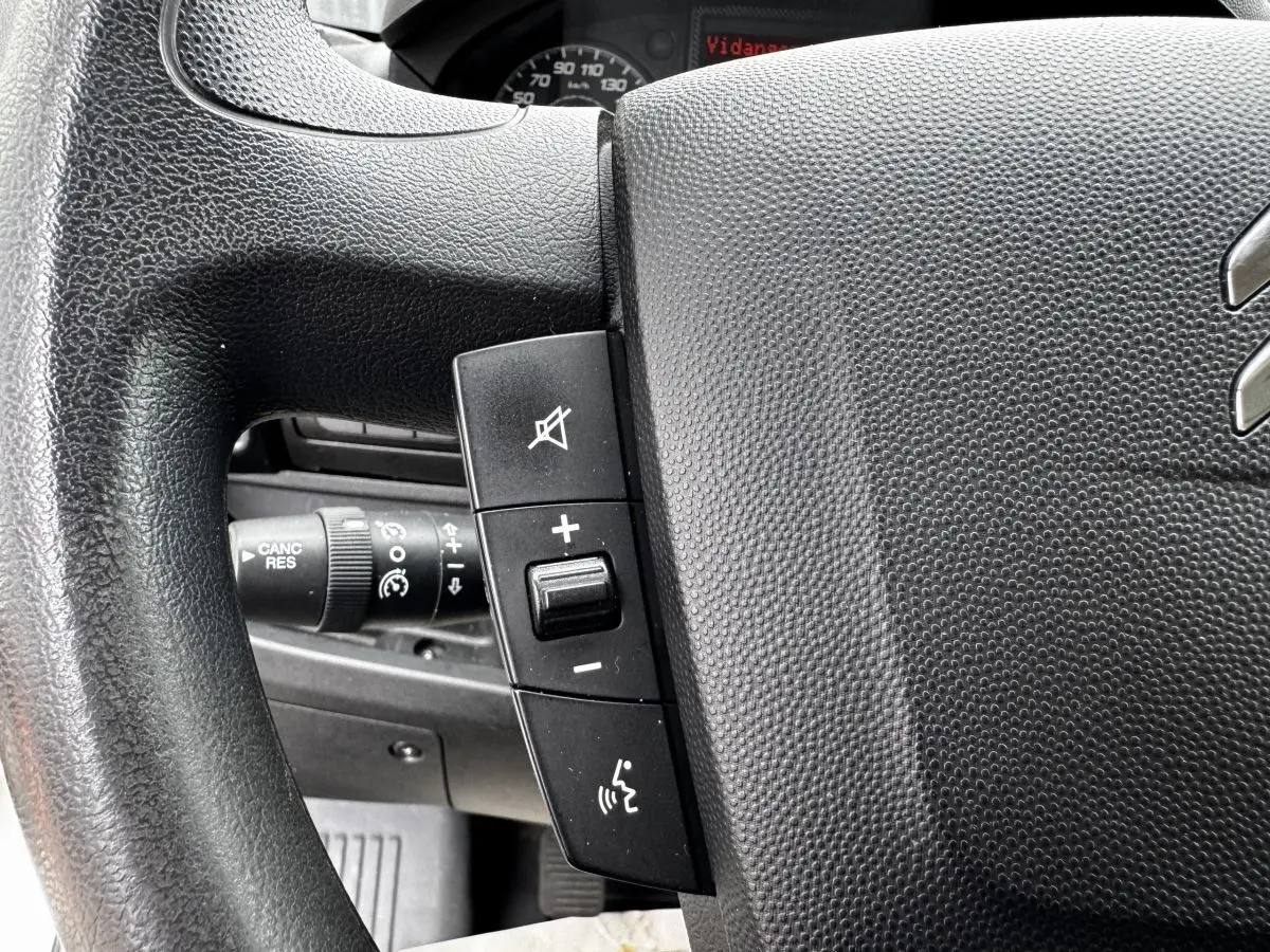 Gros plan sur le volant multifonctions noir du Citroën Jumper blanc, avec commandes de volume et de téléphone visibles.