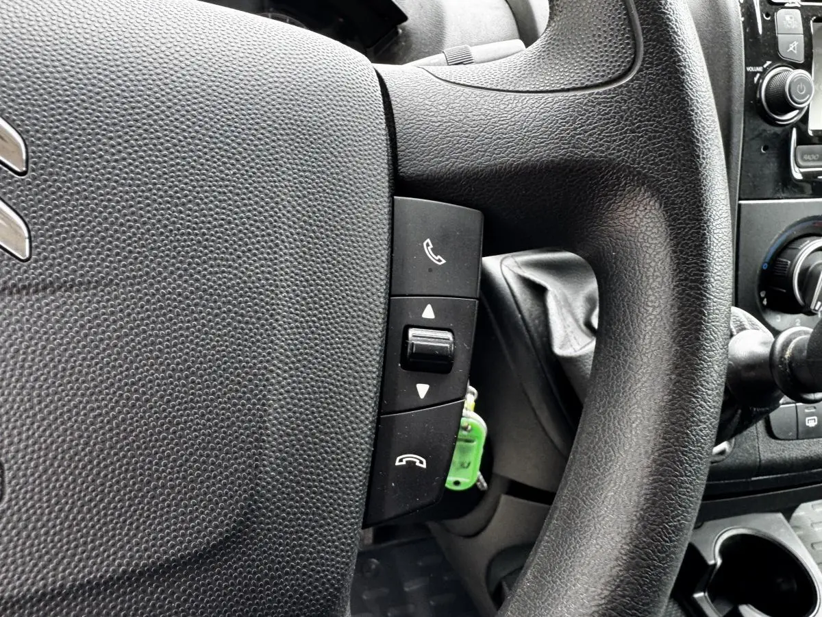 Gros plan sur le volant multifonctions noir du Citroën Jumper blanc, avec commandes d’appel téléphonique visibles.