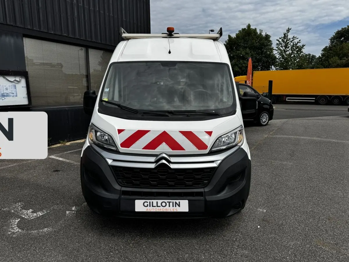 Vue avant d'un Citroën Jumper blanc avec marquage rouge et blanc en chevrons sur le capot, stationné sur un parking.