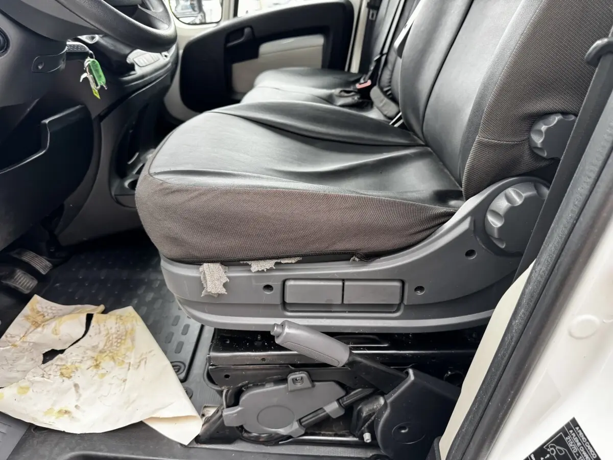 Vue intérieure côté conducteur du siège avant noir usé du Citroën Jumper blanc de 2019 avec levier de frein à main visible.