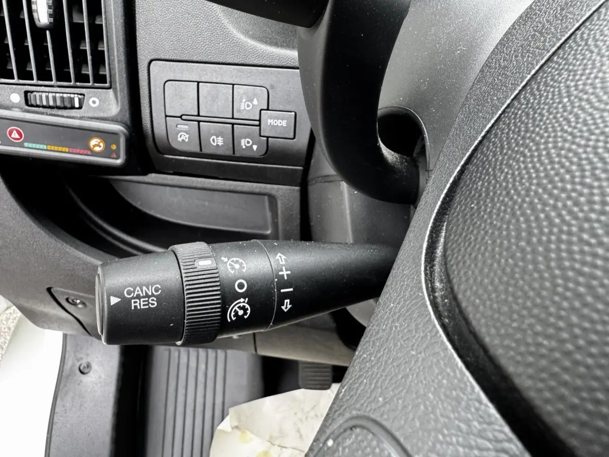 Gros plan sur la commande de régulateur de vitesse à gauche du volant dans l’habitacle du Citroën Jumper blanc.